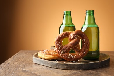 Photo of Tasty pretzels and bottles of beer on wooden table against beige gradient background, closeup. Space for text