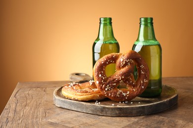 Photo of Tasty pretzels and bottles of beer on wooden table against beige gradient background, closeup
