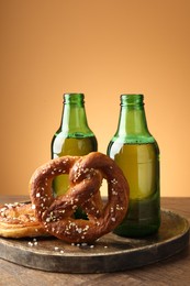 Photo of Tasty pretzels and bottles of beer on wooden table against beige gradient background, closeup
