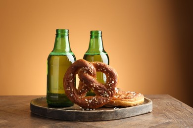 Photo of Tasty pretzels and bottles of beer on wooden table against beige gradient background, closeup