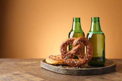 Photo of Tasty pretzels and bottles of beer on wooden table against beige gradient background, closeup. Space for text