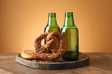 Photo of Tasty pretzels and bottles of beer on wooden table against beige gradient background, closeup