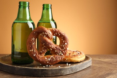 Photo of Tasty pretzels and bottles of beer on wooden table against beige gradient background, closeup