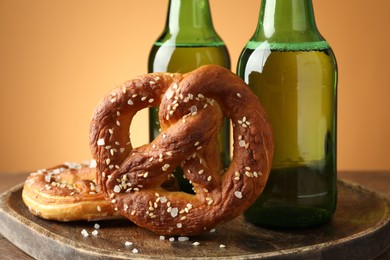 Photo of Tasty pretzels and bottles of beer on wooden table against beige gradient background, closeup
