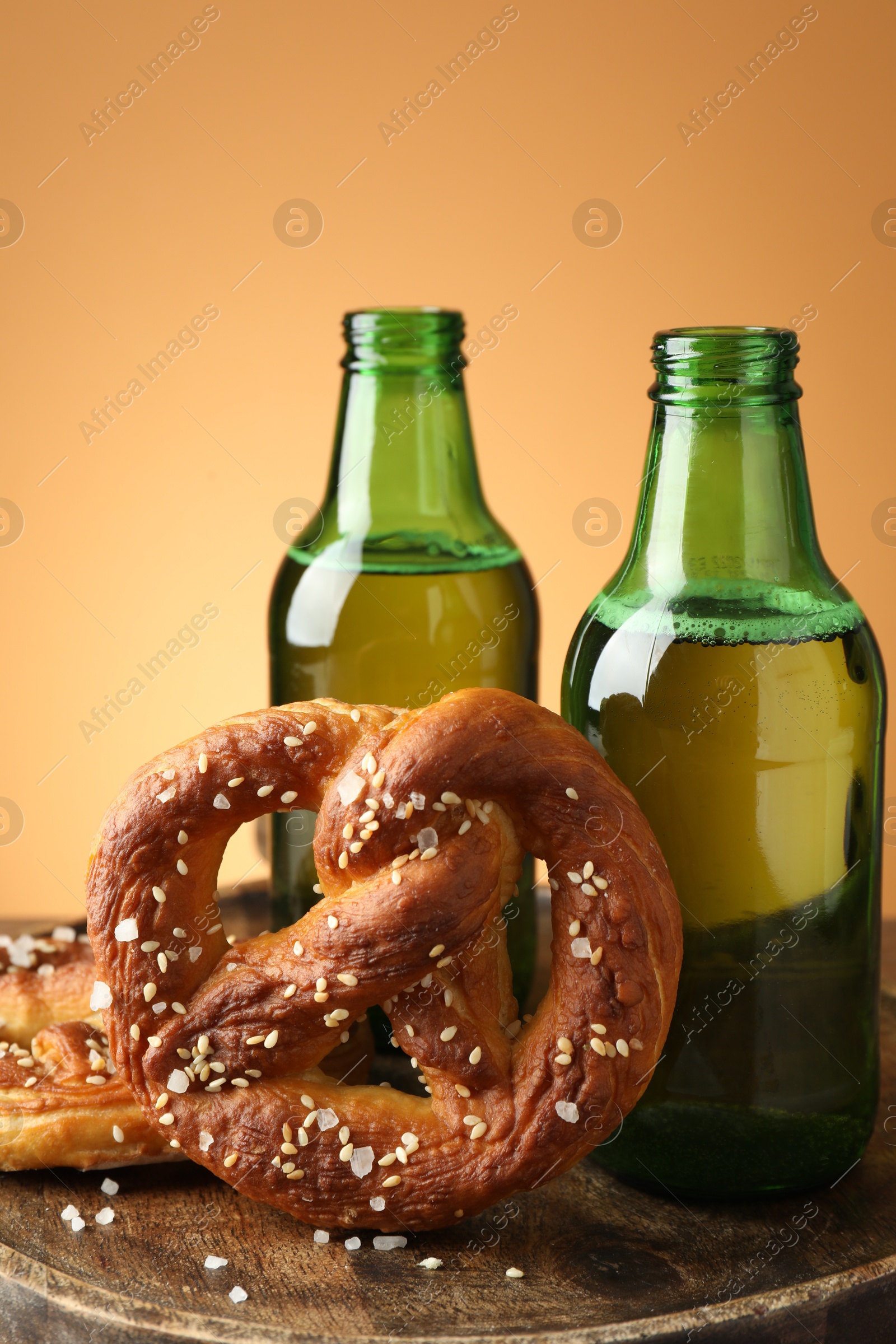 Tasty pretzels and bottles of beer on wooden board against beige gradient background, closeup Photo of Tasty pretzels and bottles of beer on wooden board against beige gradient background, closeup