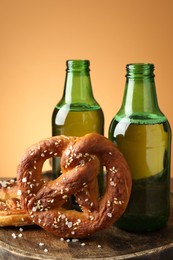 Photo of Tasty pretzels and bottles of beer on wooden board against beige gradient background, closeup