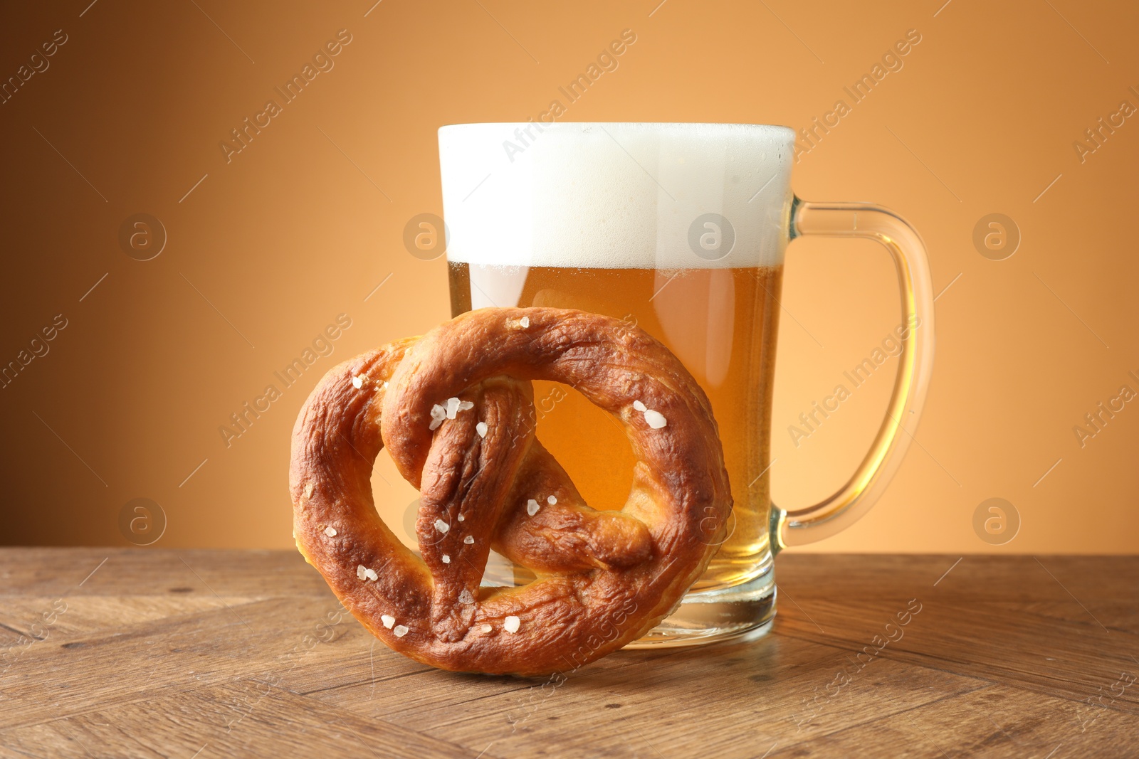Tasty pretzel and glass mug of beer on wooden table against beige gradient background, closeup Photo of Tasty pretzel and glass mug of beer on wooden table against beige gradient background, closeup