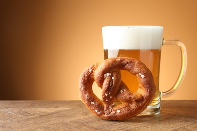 Photo of Tasty pretzel and glass mug of beer on wooden table against beige gradient background, closeup. Space for text