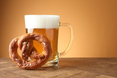 Photo of Tasty pretzel and glass mug of beer on wooden table against beige gradient background, closeup. Space for text