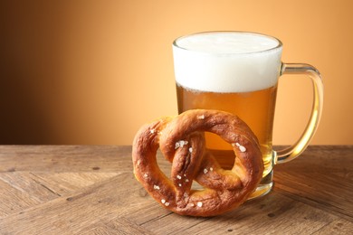 Photo of Tasty pretzel and glass mug of beer on wooden table against beige gradient background, closeup. Space for text