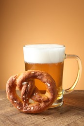 Photo of Tasty pretzel and glass mug of beer on wooden table against beige gradient background, closeup