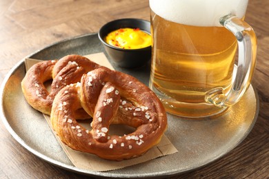Photo of Tasty pretzels, sauce and glass mug of beer on wooden table, closeup