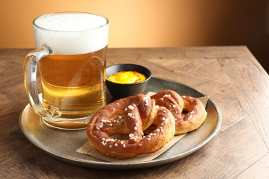 Photo of Tasty pretzels, sauce and glass mug beer on wooden table against beige gradient background, closeup