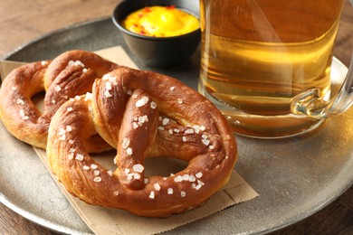 Photo of Tasty pretzels, sauce and glass of beer on wooden table, closeup