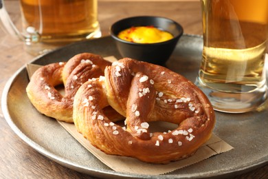 Photo of Tasty pretzels, sauce and glasses of beer on wooden table, closeup