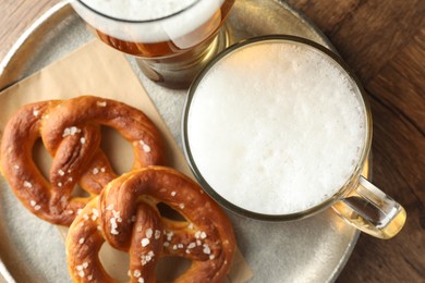 Photo of Tasty pretzels and beer on wooden table, top view