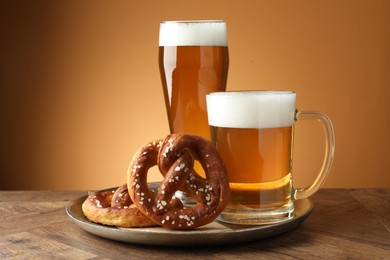 Photo of Tasty pretzels and beer on wooden table against golden gradient background, closeup