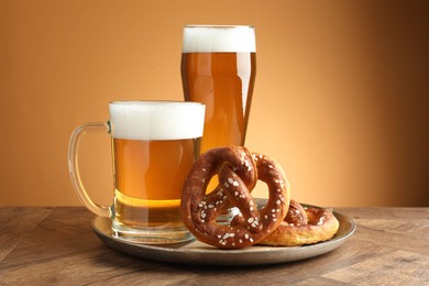 Photo of Tasty pretzels and beer on wooden table against golden gradient background, closeup