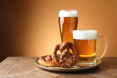 Photo of Tasty pretzels and beer on wooden table against golden gradient background, closeup