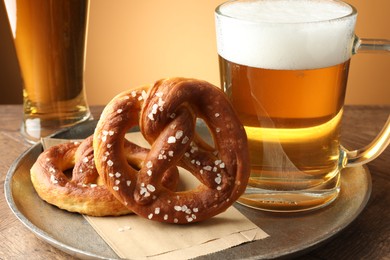 Photo of Tasty pretzels and beer on wooden table against golden gradient background, closeup
