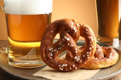 Photo of Tasty pretzels and beer on table against golden gradient background, closeup