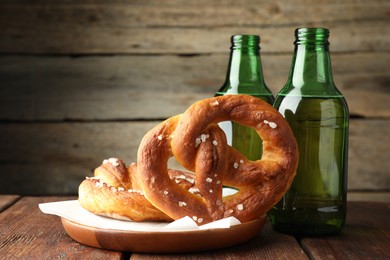 Photo of Tasty pretzels and bottles of beer on wooden table, closeup