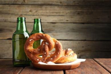 Photo of Tasty pretzels and bottles of beer on wooden table, closeup