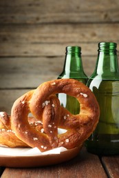 Photo of Tasty pretzels and bottles of beer on wooden table, closeup