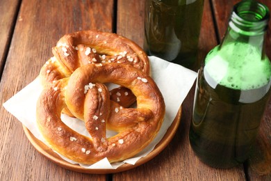 Photo of Tasty pretzels and bottles of beer on wooden table, closeup