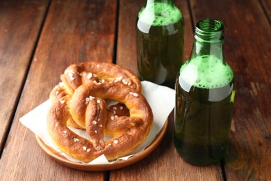 Photo of Tasty pretzels and bottles of beer on wooden table, closeup