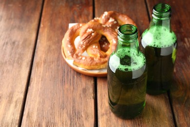Photo of Bottles of beer and tasty pretzels on wooden table, selective focus