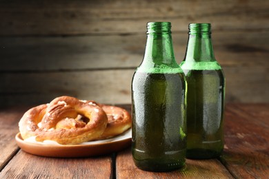Photo of Bottles of beer and tasty pretzels on wooden table, selective focus