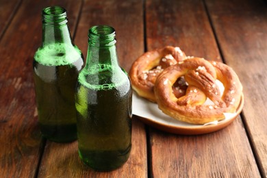 Photo of Bottles of beer and tasty pretzels on wooden table, selective focus