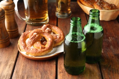 Photo of Bottles of beer and tasty pretzels on wooden table, selective focus