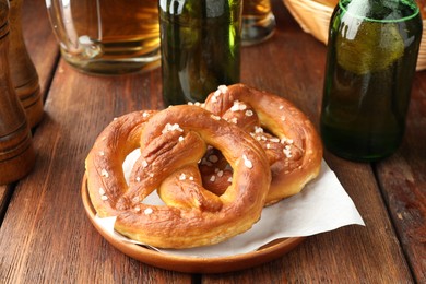 Photo of Tasty pretzels and bottles of beer on wooden table, closeup