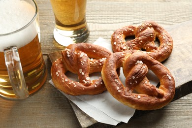 Photo of Tasty pretzels and beer on wooden table, closeup
