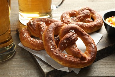Photo of Tasty pretzels and beer on wooden table, closeup