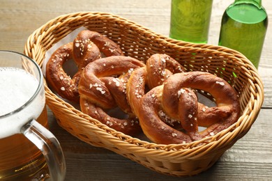 Photo of Tasty pretzels in basket and beer on wooden table, closeup