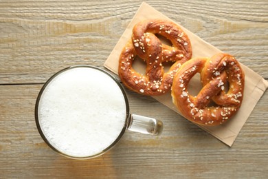 Photo of Tasty pretzels and glass mug of beer on wooden table, flat lay