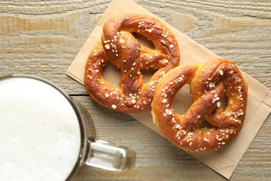 Photo of Tasty pretzels and glass mug of beer on wooden table, flat lay