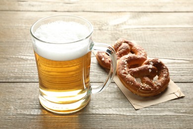 Photo of Tasty pretzels and glass mug of beer on wooden table, closeup