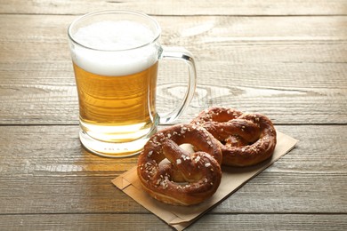 Photo of Tasty pretzels and glass mug of beer on wooden table, closeup