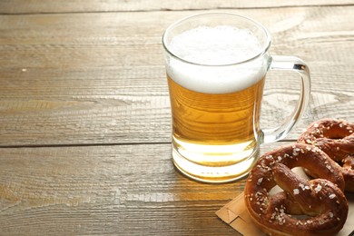 Photo of Tasty pretzels and glass mug of beer on wooden table, closeup. Space for text