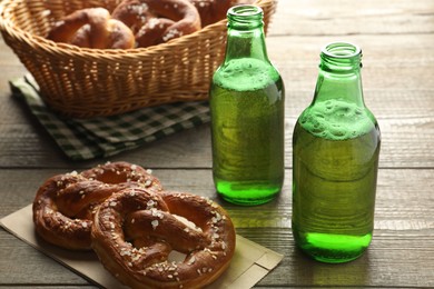 Photo of Tasty pretzels and bottles of beer on wooden table, closeup