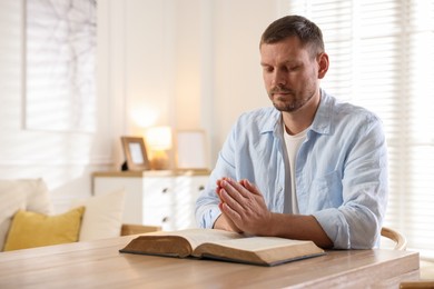 Photo of Man with Bible praying at table indoors. Space for text