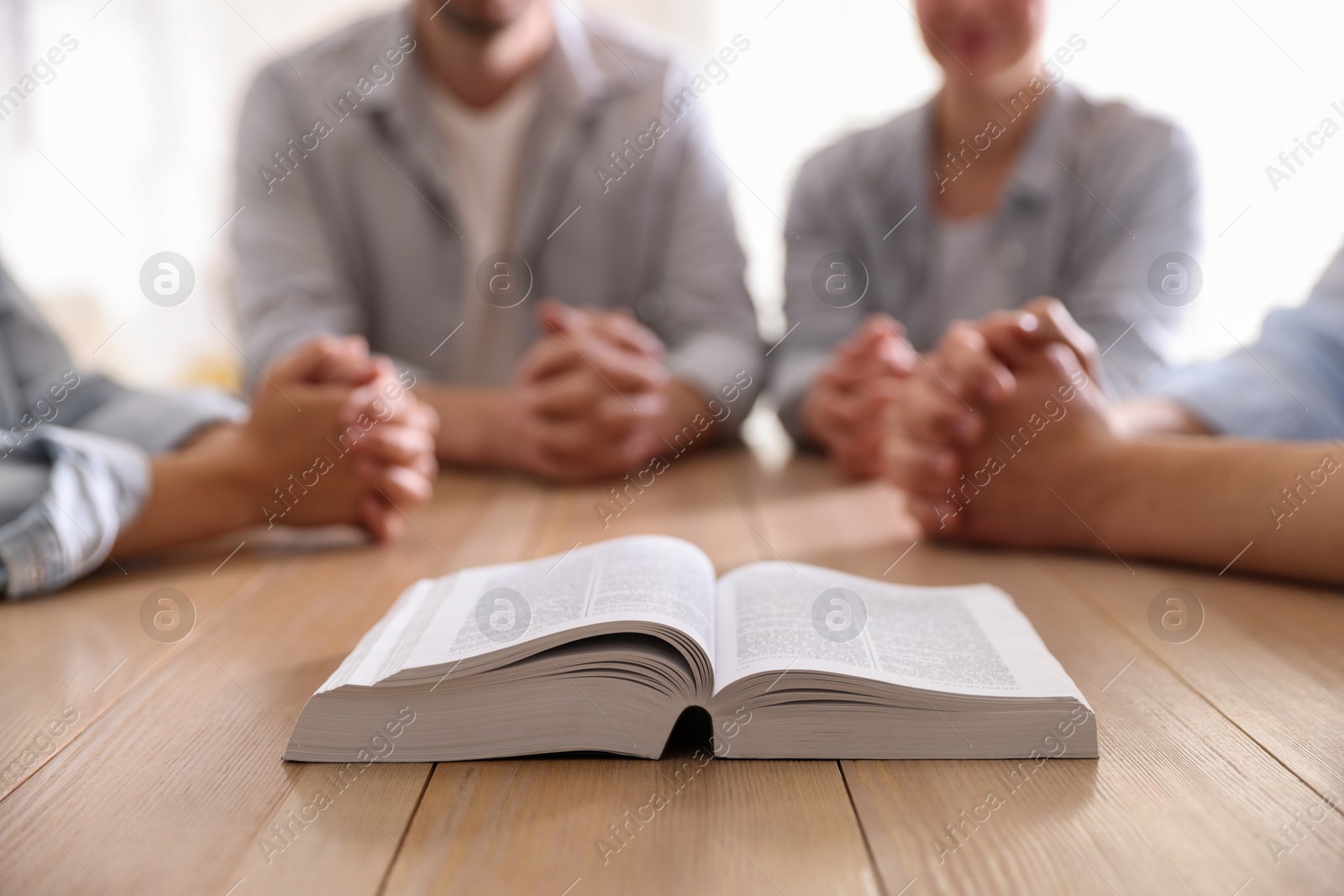 Family with Bible praying at wooden table indoors, closeup Photo of Family with Bible praying at wooden table indoors, closeup