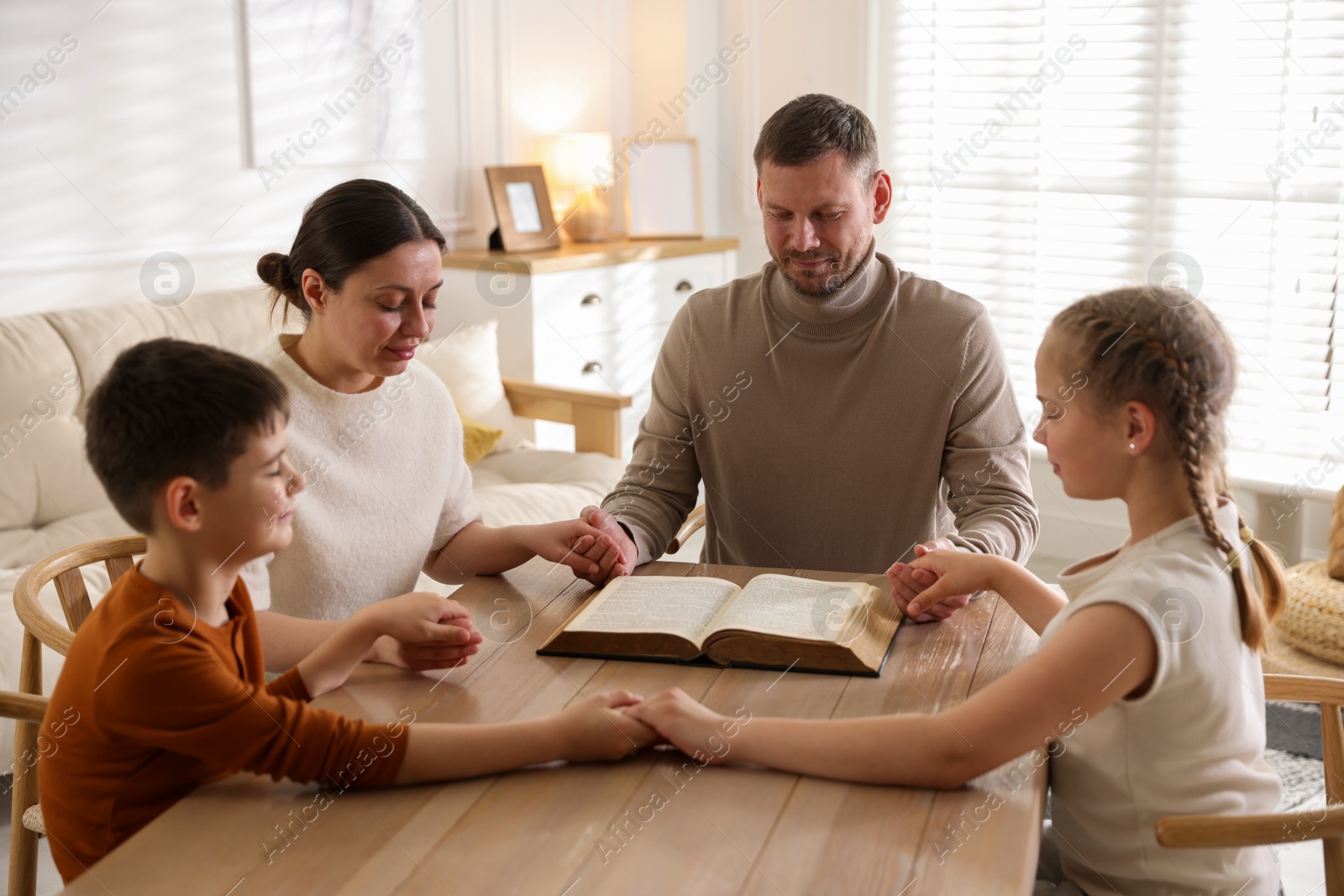 Family with Bible praying at table indoors Photo of Family with Bible praying at table indoors