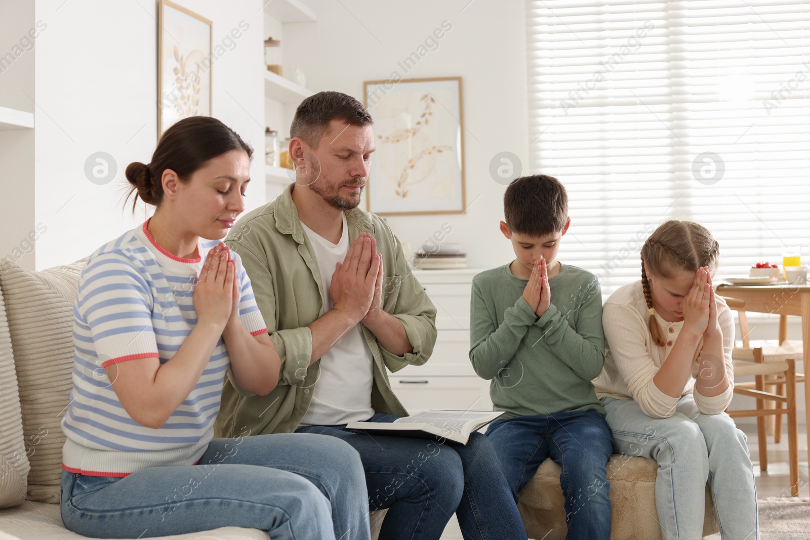 Family with Bible praying together at home Photo of Family with Bible praying together at home