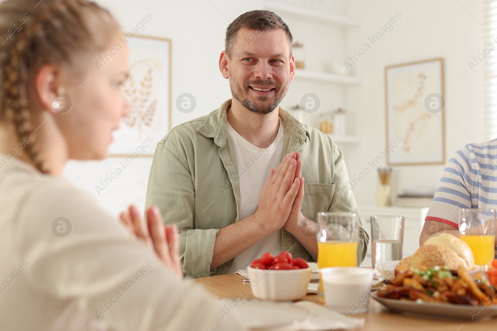 Family praying together before dinner at table indoors Photo of Family praying together before dinner at table indoors