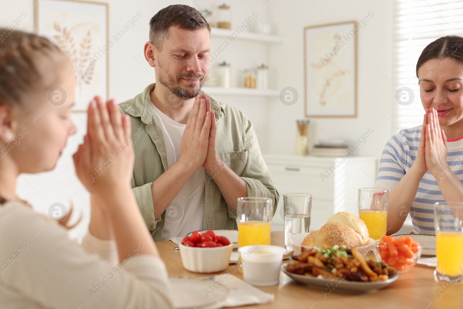 Family praying together before dinner at table indoors Photo of Family praying together before dinner at table indoors